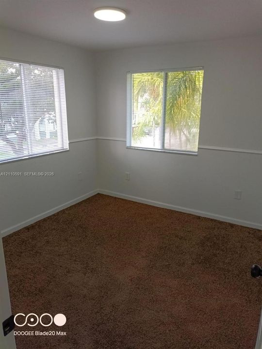 Interior room featuring neutral-toned carpeting, two dual-pane windows with horizontal blinds, wall-mounted chair rail molding, and a flush-mount overhead light fixture