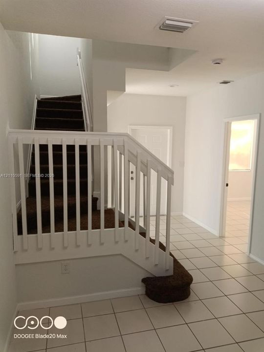Staircase featuring dark carpeted treads and white wooden balustrade, complemented by neutral tile flooring