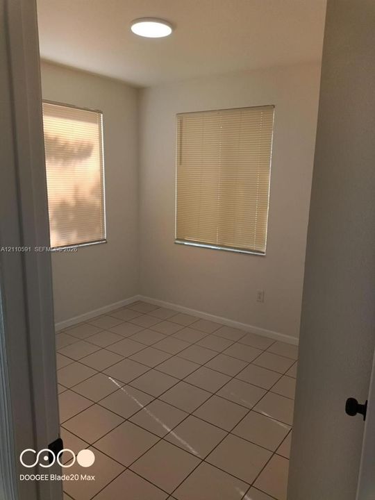 Interior room featuring neutral-toned tile flooring, two windows with horizontal blinds, and a flush-mount circular ceiling light