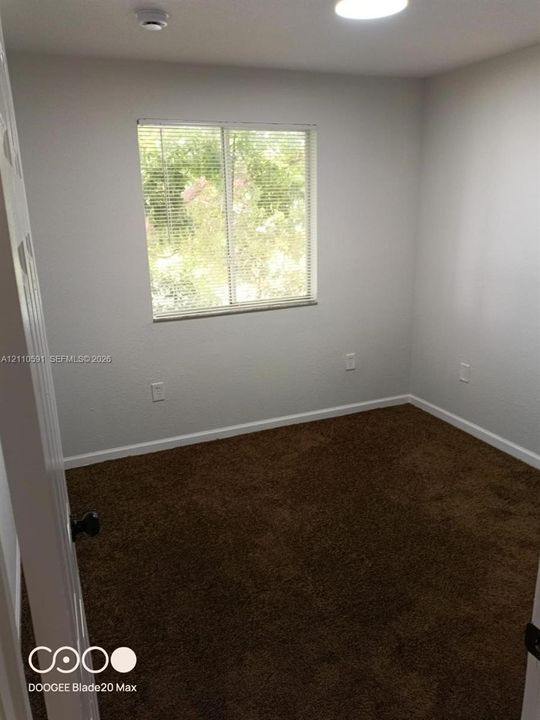 Neutral interior space featuring carpeting, smooth-finish walls, a single-pane sliding window with integrated blinds, and a ceiling-mounted light fixture