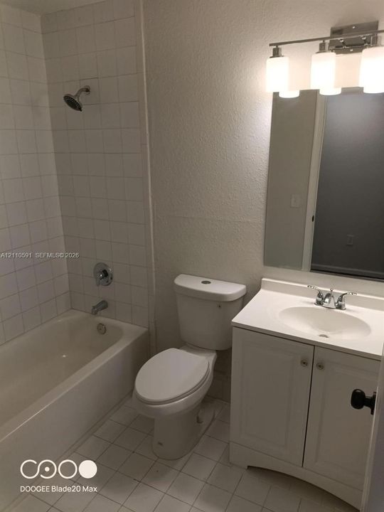 Bathroom featuring a white vanity cabinet with an integrated basin, three-light wall fixture, framed mirror, and tiled shower surround with a built-in tub