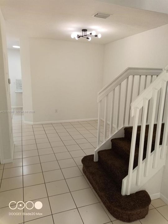 Staircase featuring a white balustrade with brown carpeted treads, complemented by neutral tile flooring and a multi-arm architectural light fixture
