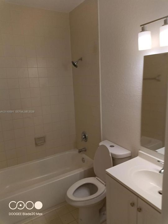 Bathroom featuring a white vanity cabinet with an integrated sink, a rectangular wall-mounted mirror, a two-light fixture, and a tub with tiled surround