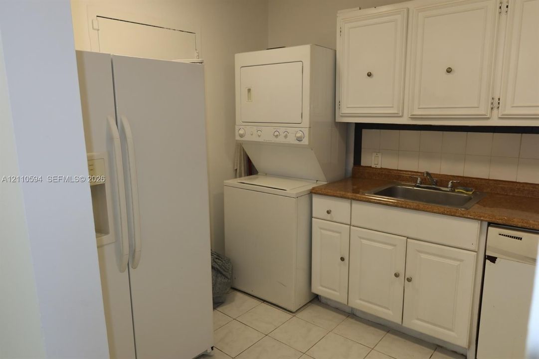Utility space featuring white cabinetry, stone-finish countertops, stainless steel sink with a dual-handle faucet, tile flooring, and built-in laundry appliances