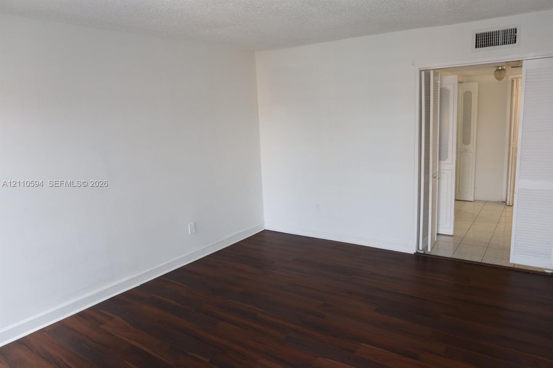 Room featuring wood-finish flooring, white walls, and dual-panel louvered closet doors