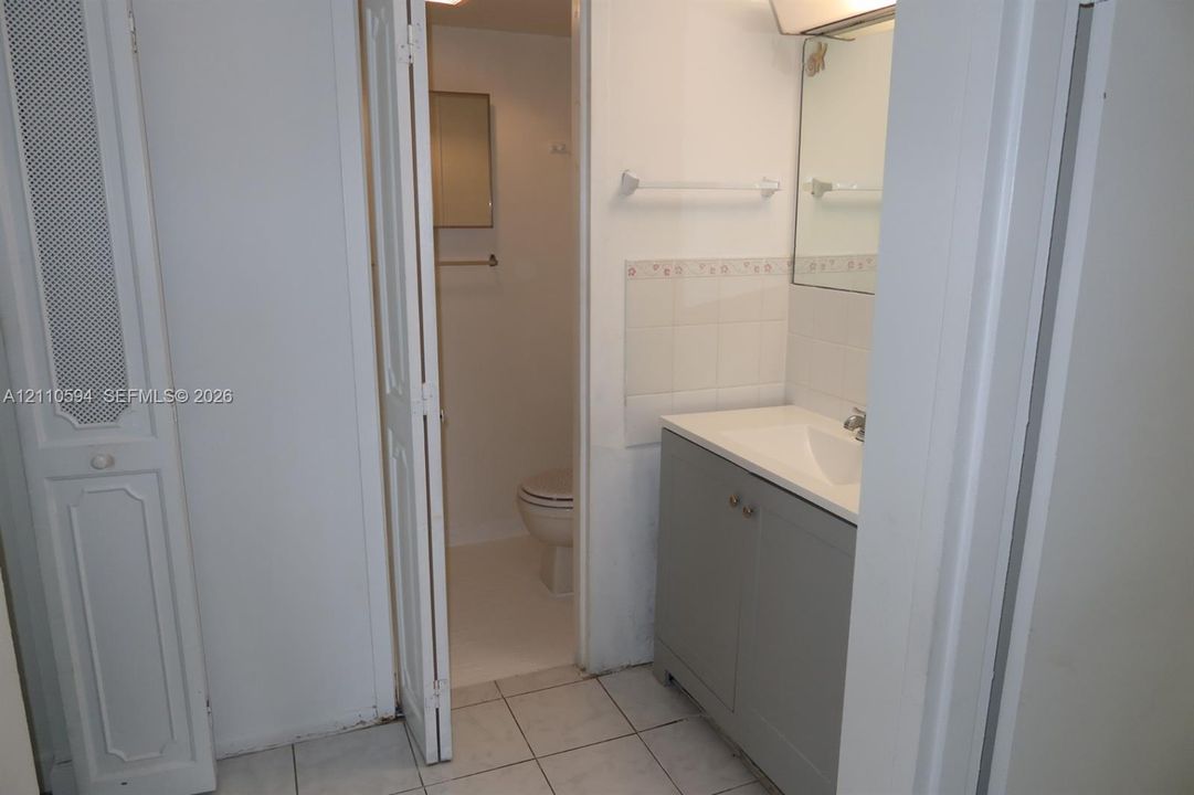 Bathroom featuring a gray vanity cabinet with a white countertop, wall-mounted mirror, ceramic tile flooring, and bi-fold closet doors
