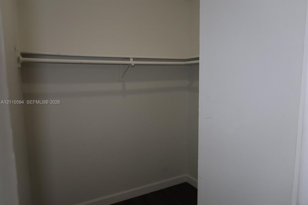 Storage closet featuring neutral-toned walls, wood-finish flooring, and a built-in horizontal rod and shelf
