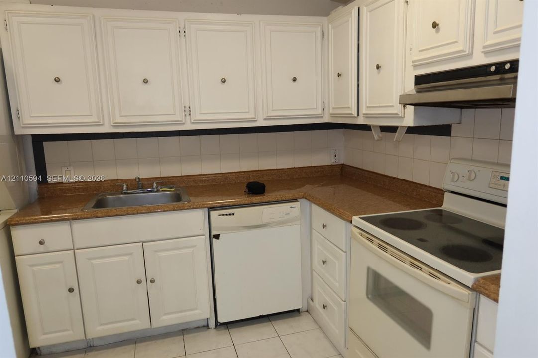 Kitchen featuring white cabinetry, stone-finish countertops, tile backsplash, stainless steel sink with faucet, and built-in dishwasher