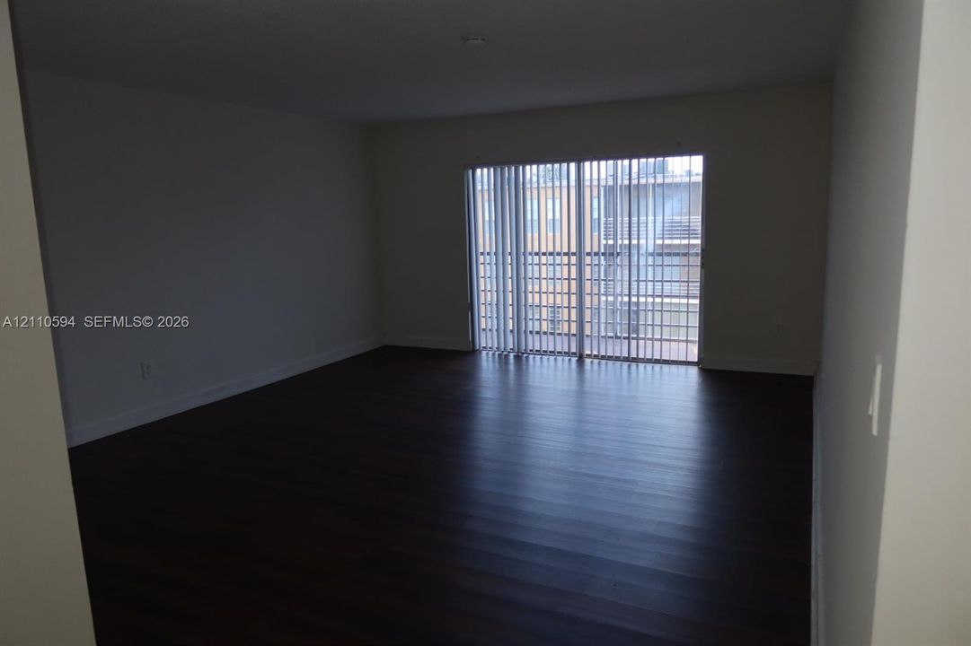 Interior space featuring wood-finish flooring, neutral wall tones, and glass sliding doors with vertical blinds