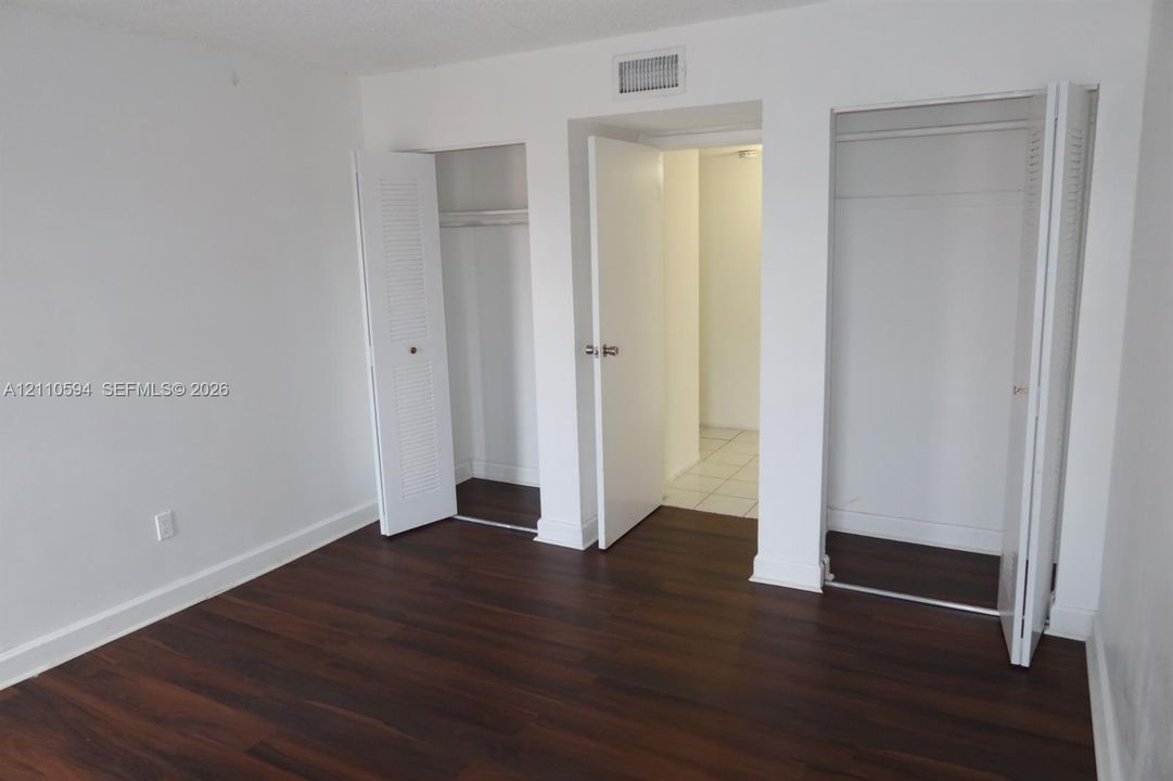 Room featuring wood-finish flooring, white walls, and two closets with bi-fold doors