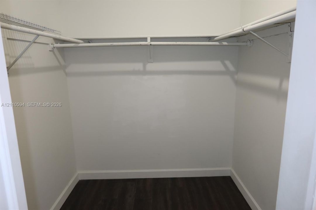 Walk-in storage space featuring wood-finish flooring and integrated wire shelving with hanging rods