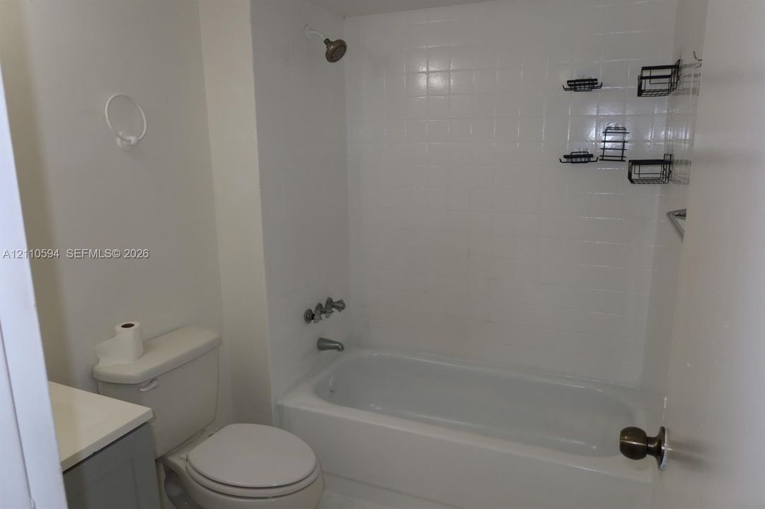 Bathroom featuring a white bathtub with a tiled surround, chrome plumbing fixtures, a vanity with a solid-surface countertop, and a white toilet