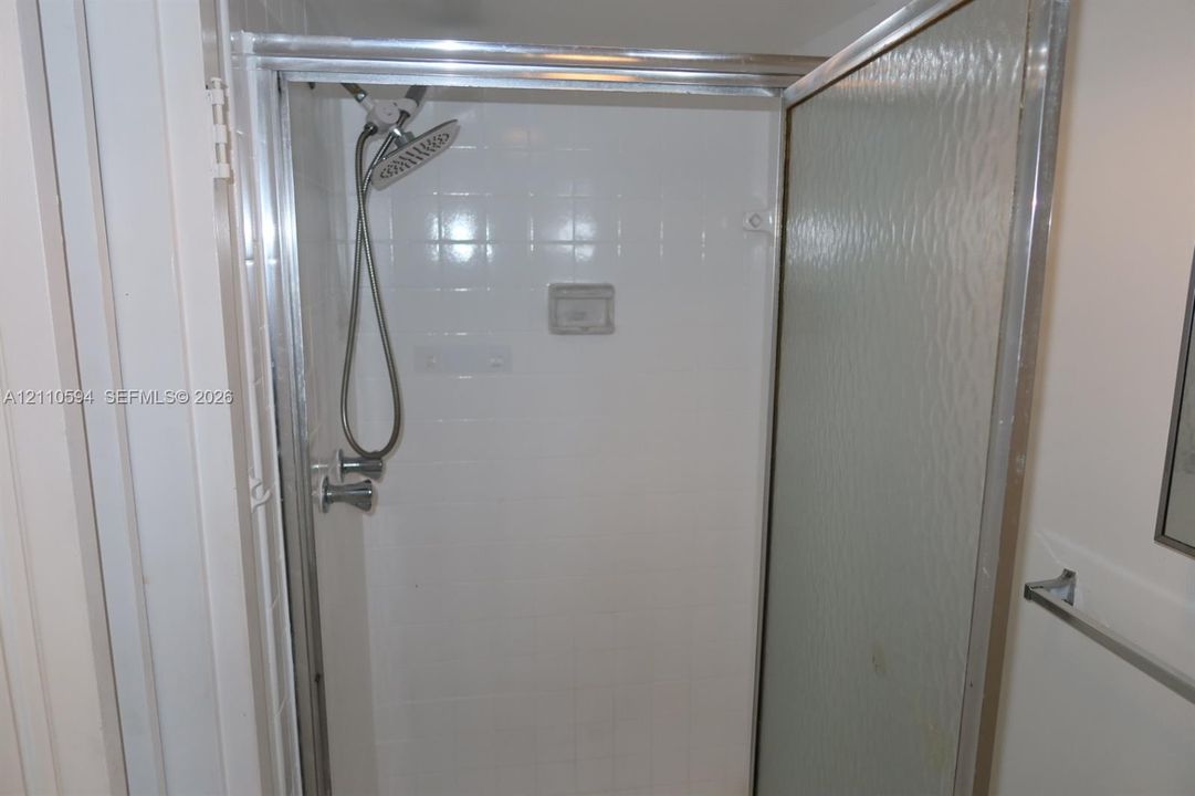 Shower stall featuring white wall tile, a chrome handheld shower head, a built-in recessed soap niche, and a glass-paneled door with a chrome frame
