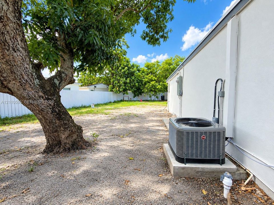 Exterior space featuring a white privacy fence, mature tree, and exterior HVAC unit