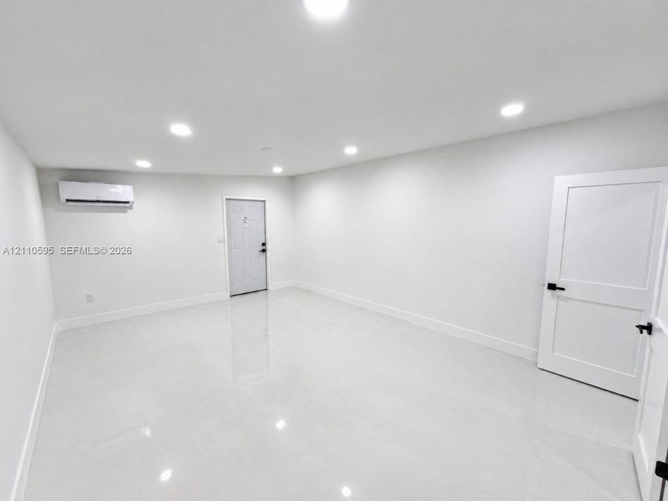 Polished tile flooring, recessed ceiling lighting, wall-mounted ductless heating and cooling unit, and solid-core paneled doors with matte black hardware