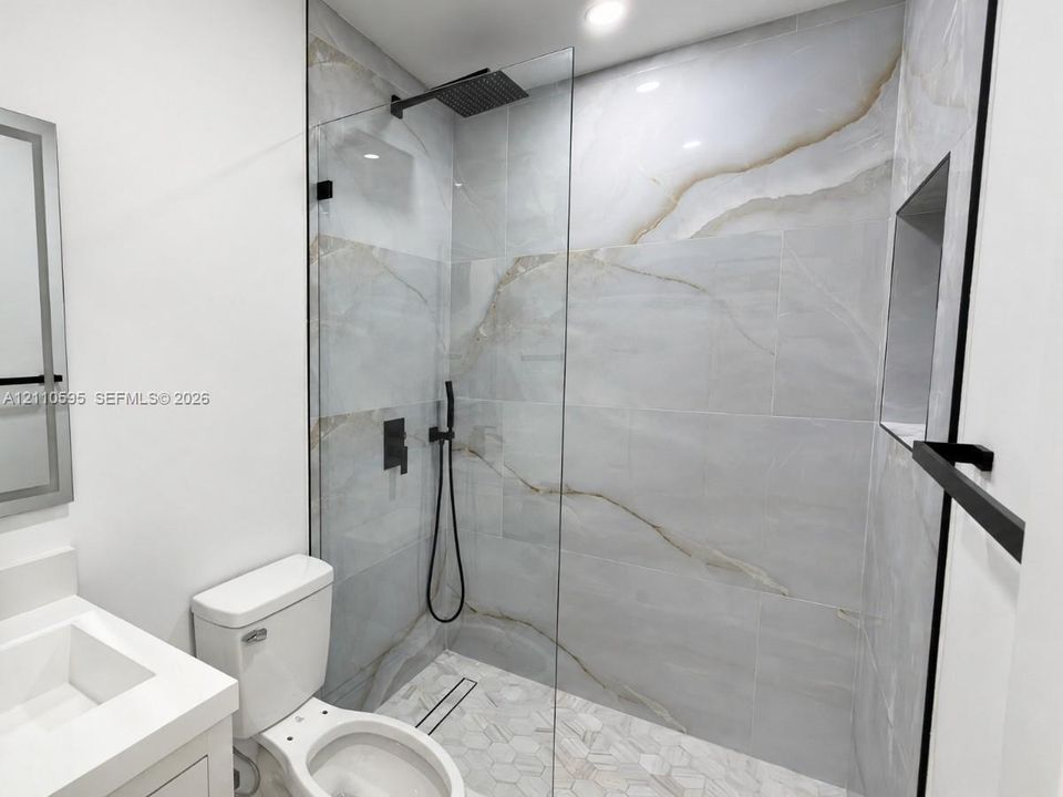 Walk-in shower featuring floor-to-ceiling large-format tile, glass panel enclosure, matte black rainfall showerhead with handheld attachment, and built-in recessed niche