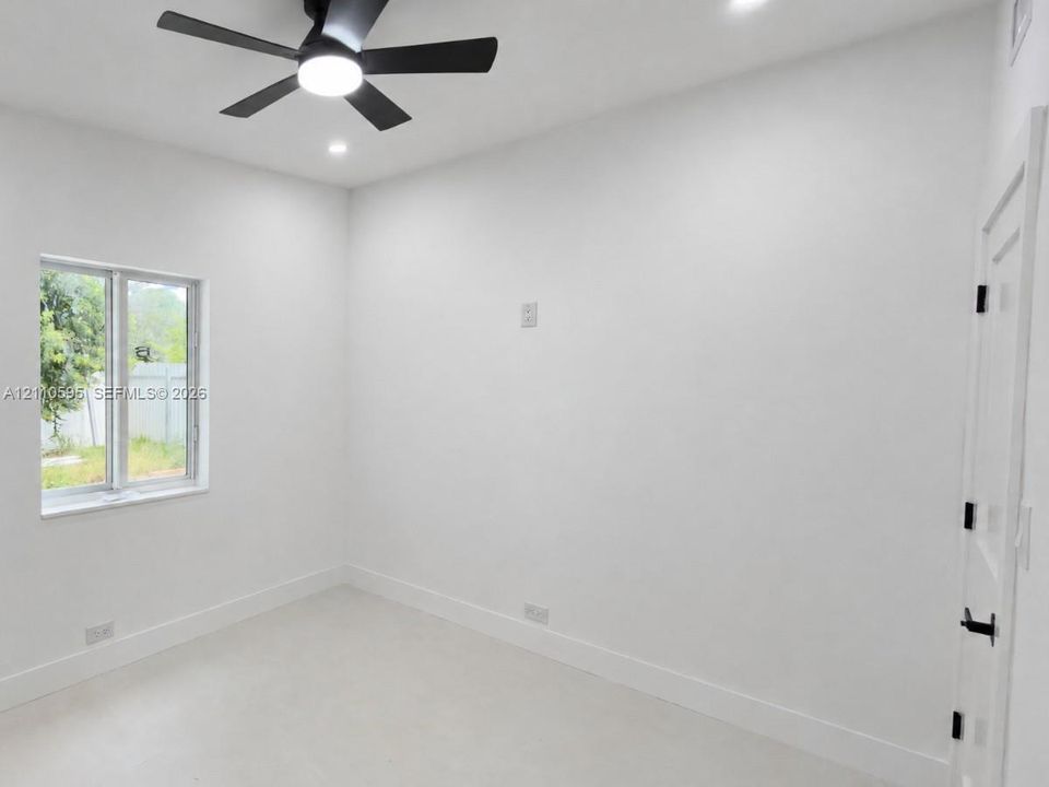 Interior room featuring smooth white walls, recessed ceiling lighting, a matte black multi-blade ceiling fan with integrated lighting, a single-hung window, and a door with matte black hardware