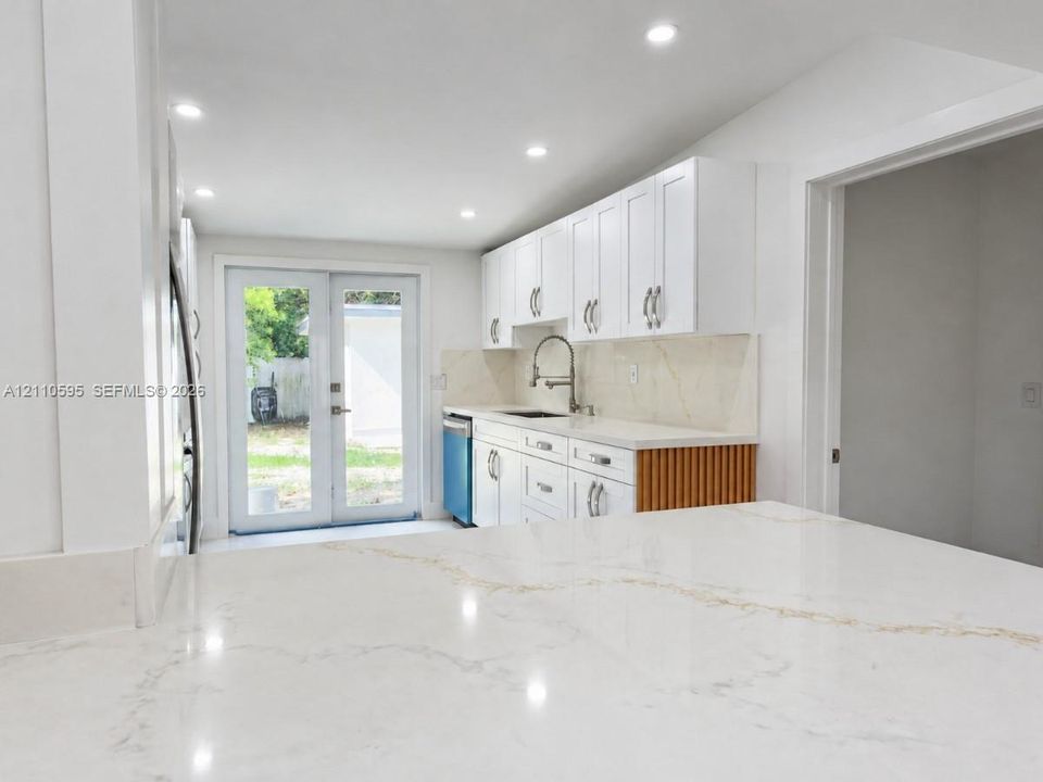 Kitchen featuring white shaker-style cabinetry, stone-surface countertops with integrated backsplash, recessed lighting, and glass-paneled French doors