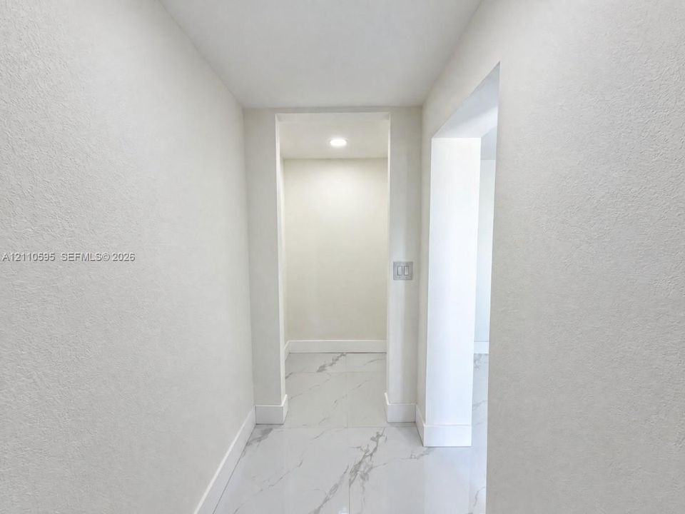 Neutral-toned interior hall featuring light-colored stone-finish flooring with veining, recessed ceiling lighting, and smooth-finish walls