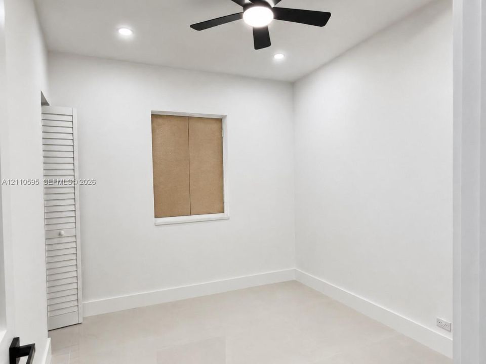 Interior space featuring neutral tile flooring, a matte black ceiling fan with integrated lighting, recessed lighting, and a closet with white louvered doors