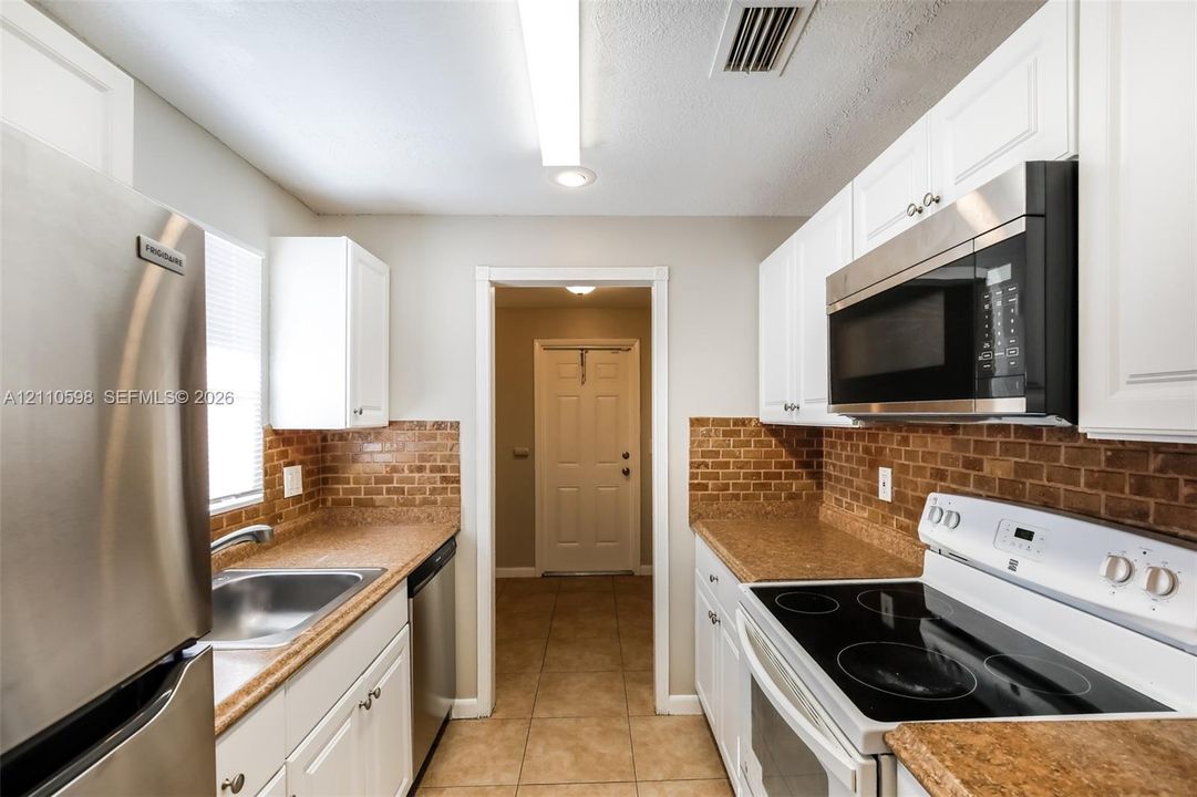 Kitchen featuring white cabinetry, stone-finish countertops, brick-style tile backsplash, and stainless steel appliances