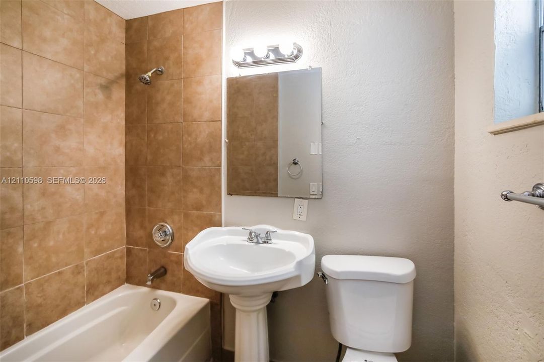Full bathroom featuring a white pedestal sink, tiled shower surround, integrated bathtub, wall-mounted medicine cabinet, and three-light vanity fixture