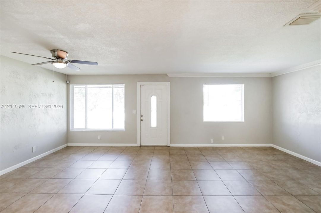 Interior space featuring ceramic tile flooring, neutral wall tones, a ceiling fan with integrated lighting, and multiple windows