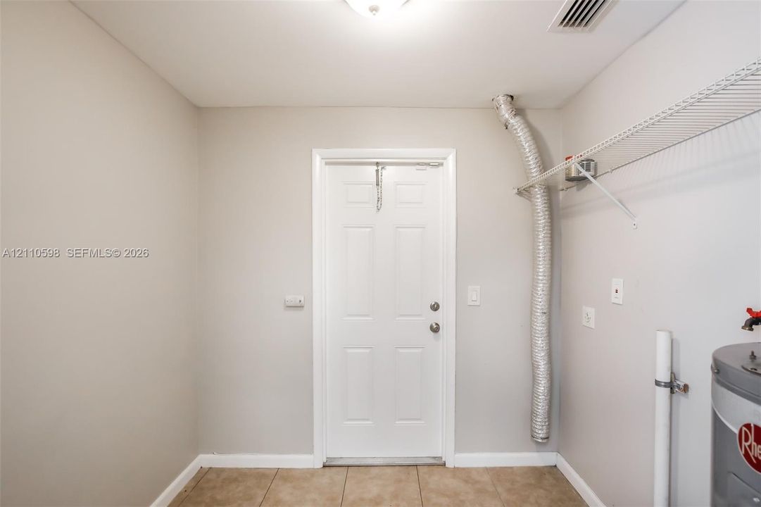 Utility area featuring tile flooring, a six-panel door, built-in wire shelving, and an integrated water heating unit