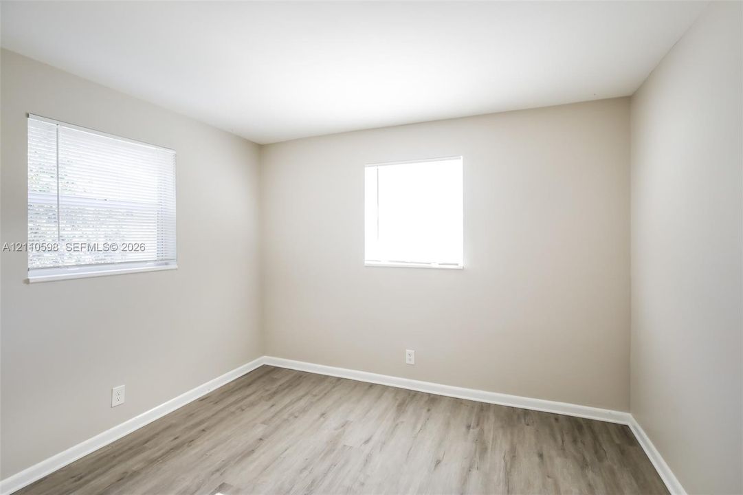 Neutral-toned interior space featuring wood-finish flooring, two windows with horizontal blinds, and smooth-finish wall surfaces