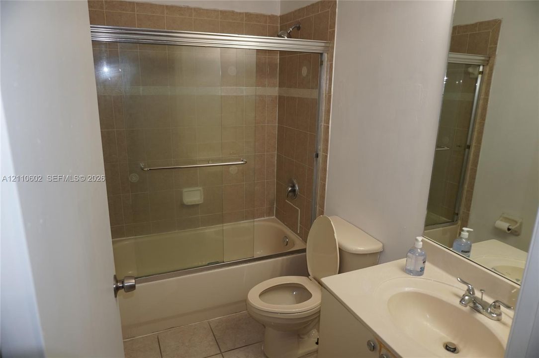 Bathroom featuring a tub-shower combination with glass sliding doors, ceramic tile shower surround, integrated sink vanity, and tile flooring