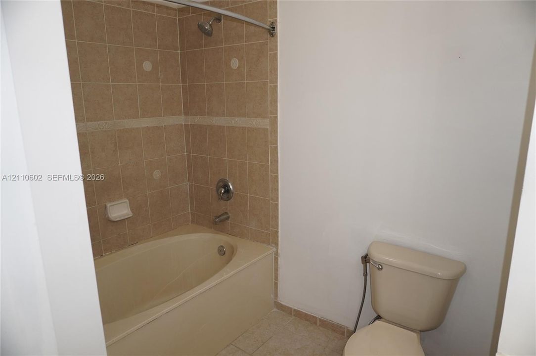 Full-size tub and shower combination featuring neutral-toned tile surround, built-in soap niche, and chrome plumbing fixtures