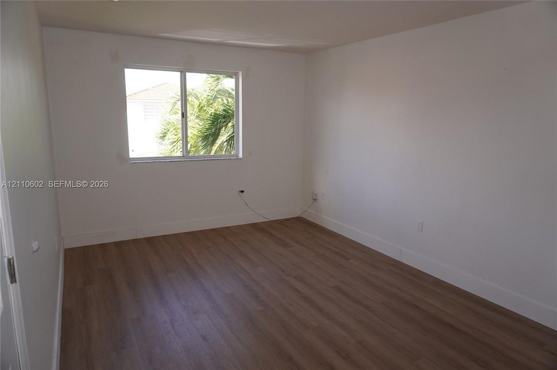 Room featuring wood-finish flooring, white walls, and a sliding window