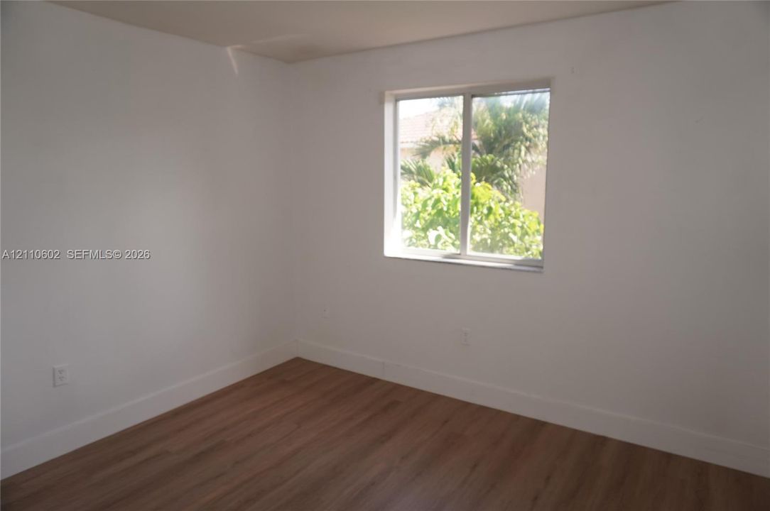 Room featuring wood-finish flooring, white walls, and a sliding window