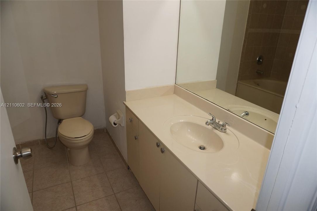 Full bathroom featuring a single-basin vanity with solid-surface countertop, inset sink, large wall-mounted mirror, and tile flooring