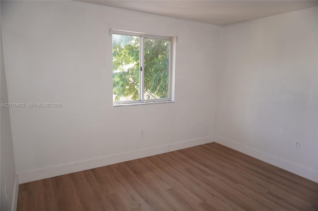 Room featuring wood-finish flooring, crisp white walls, and a single-pane sliding window