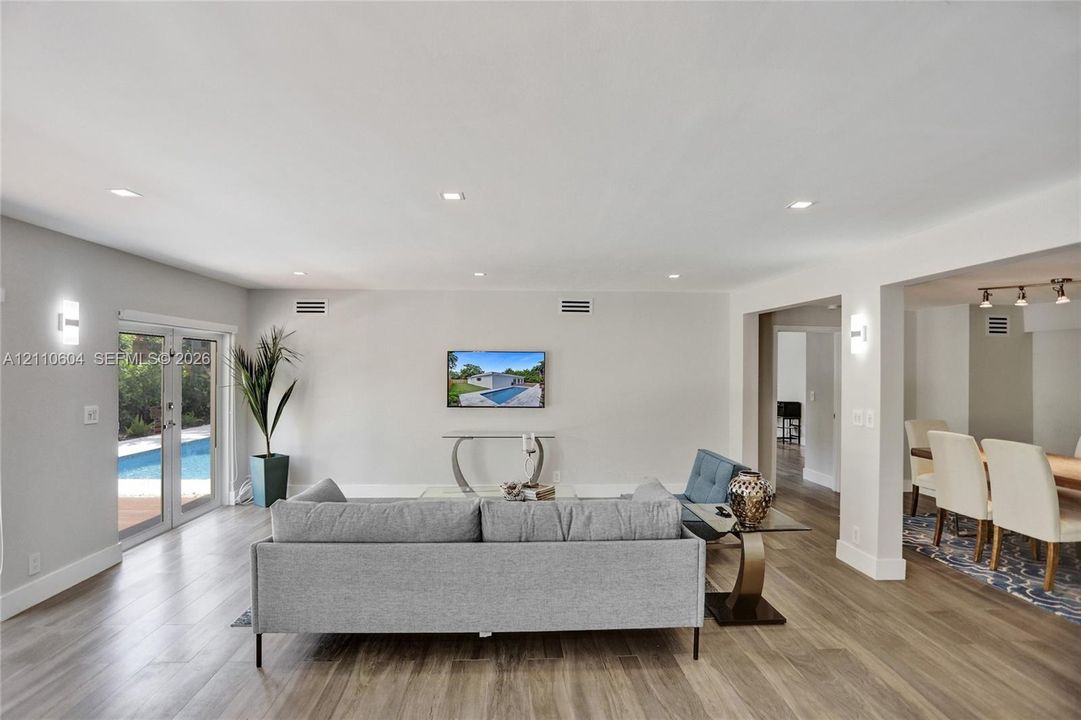 Open-concept living space featuring wood-finish flooring, recessed lighting, wall-mounted light fixtures, and glass-paned French doors with exterior patio access