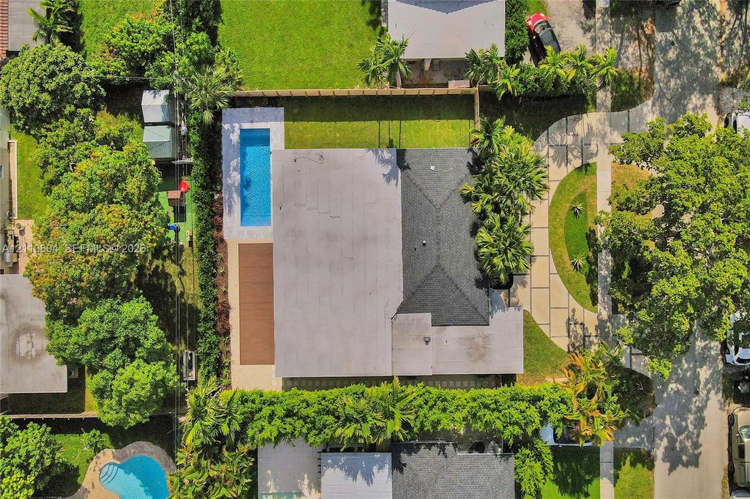 Aerial perspective of a property featuring an in-ground swimming pool, a wood-finish deck, a concrete driveway, and mature landscaping