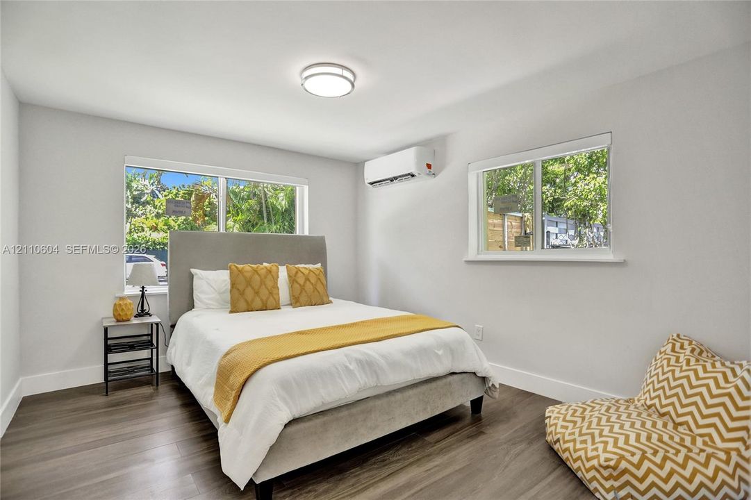 Room featuring wood-finish flooring, two sliding windows, and a wall-mounted ductless heating and cooling unit