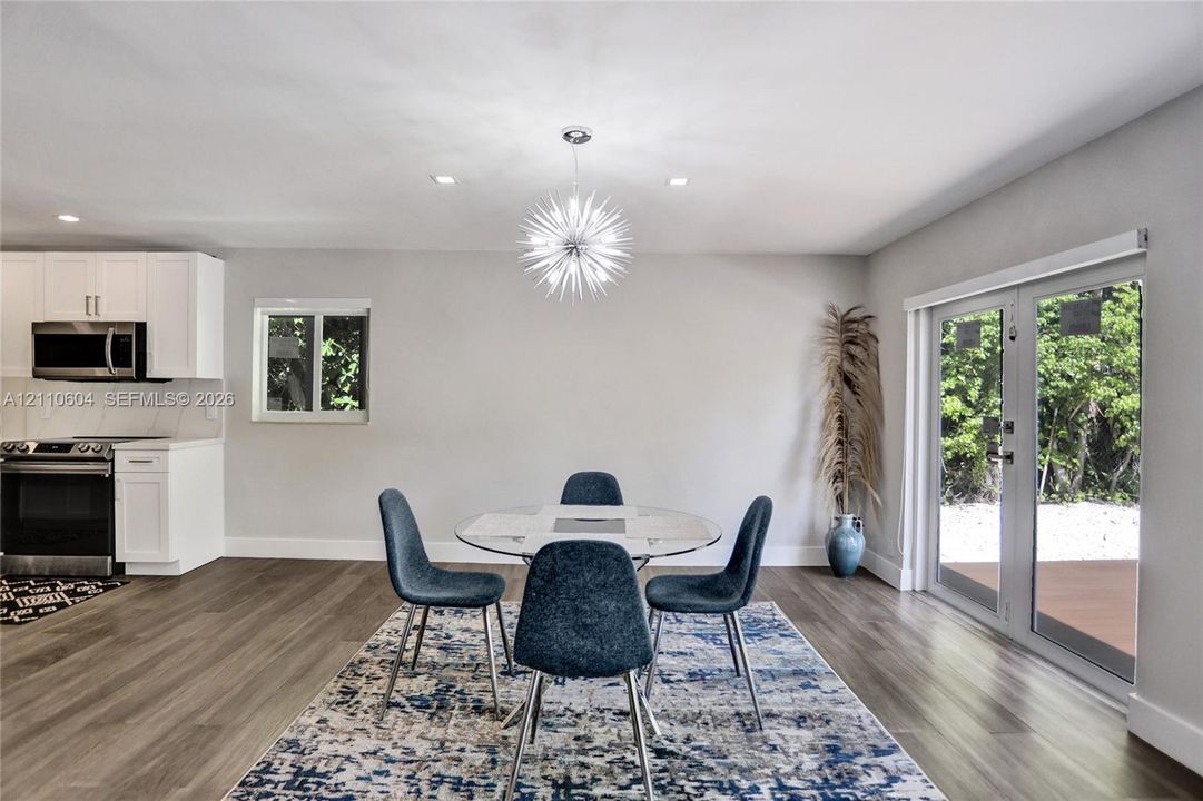 Open-concept area featuring wood-finish flooring, white cabinetry, a statement starburst chandelier, and glass double doors providing exterior access