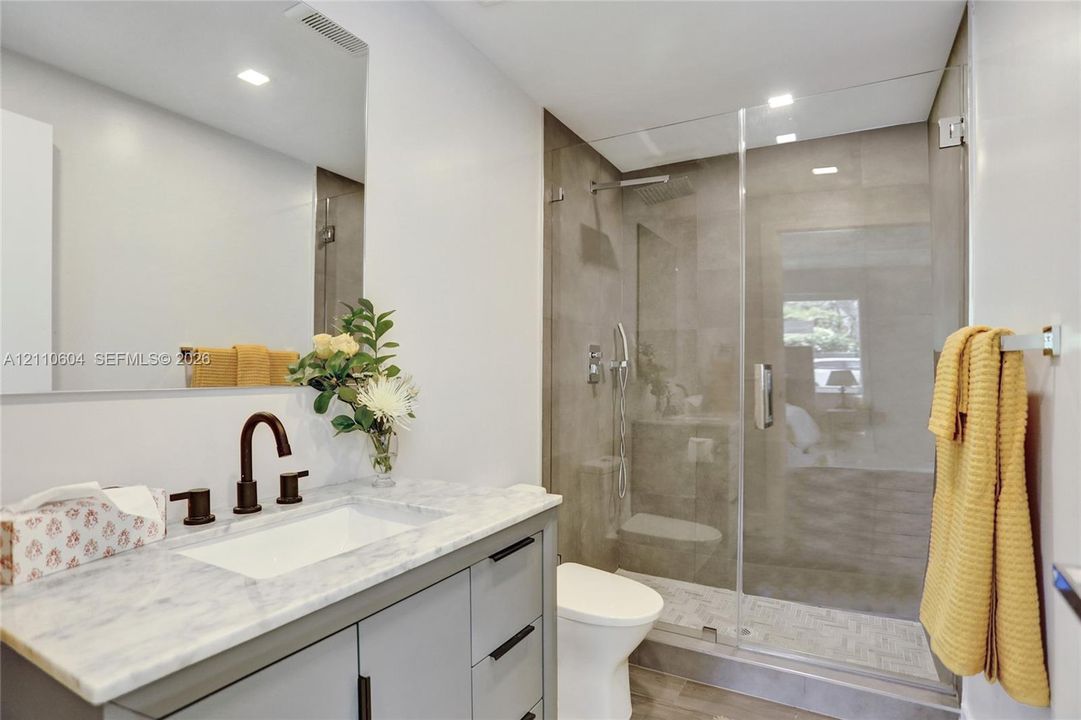 Bathroom featuring a light-toned stone-finish vanity top, undermount sink with dark metallic fixtures, a frameless glass-enclosed shower with tile surround, and recessed ceiling lighting