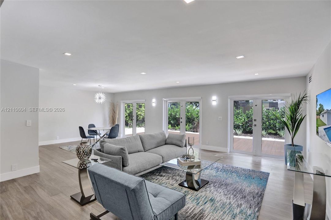 Open-concept interior featuring wood-finish flooring, recessed lighting, three sets of white-framed glass French doors, and wall-mounted light fixtures