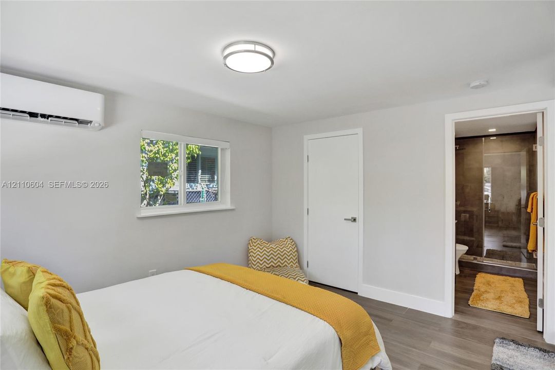 Neutral-toned interior featuring wood-finish flooring, a wall-mounted ductless climate control unit, a sliding-window, and a flush-mount ceiling light fixture