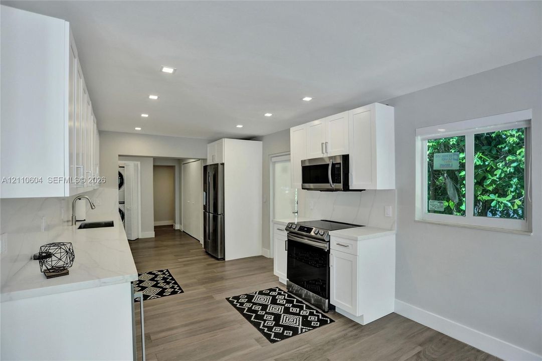 Kitchen featuring white shaker-style cabinetry, light-toned stone-finish countertops, stainless steel appliances, and wood-finish flooring