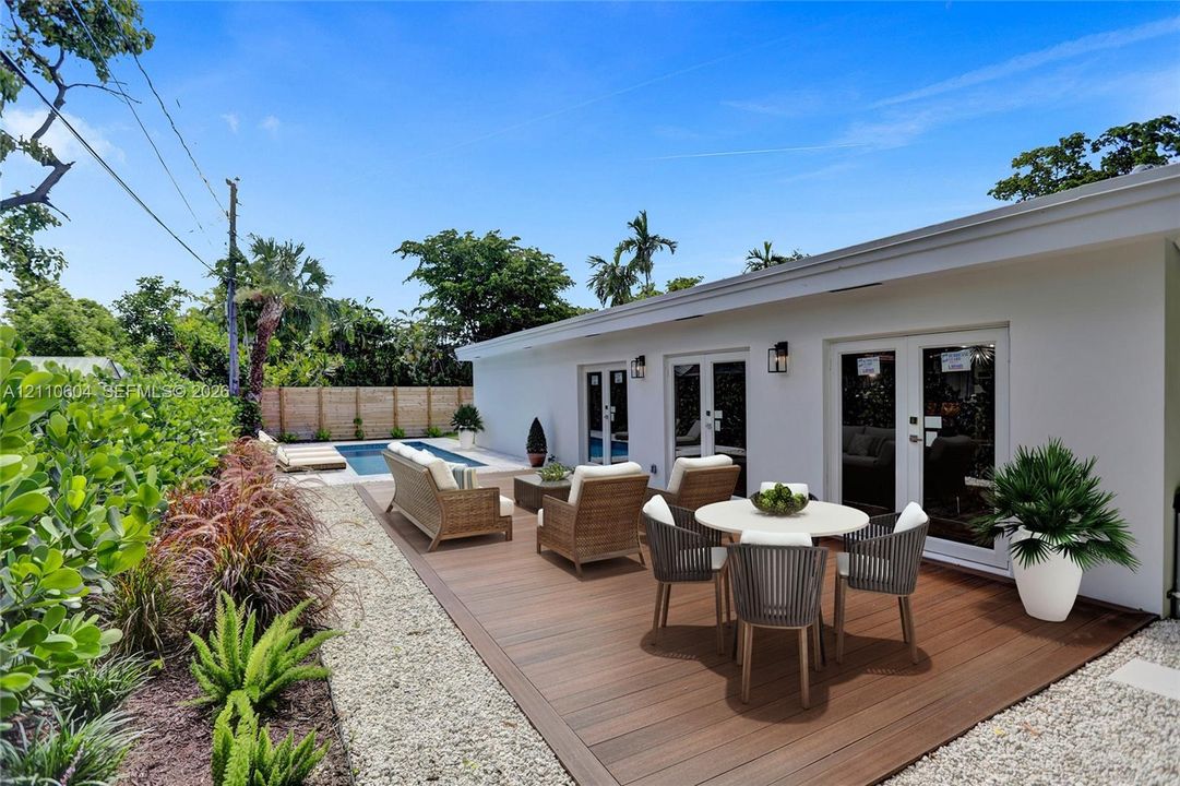 Rear outdoor area featuring a composite deck, swimming pool, gravel landscaping, exterior wall-mounted lighting, and double-door entry points