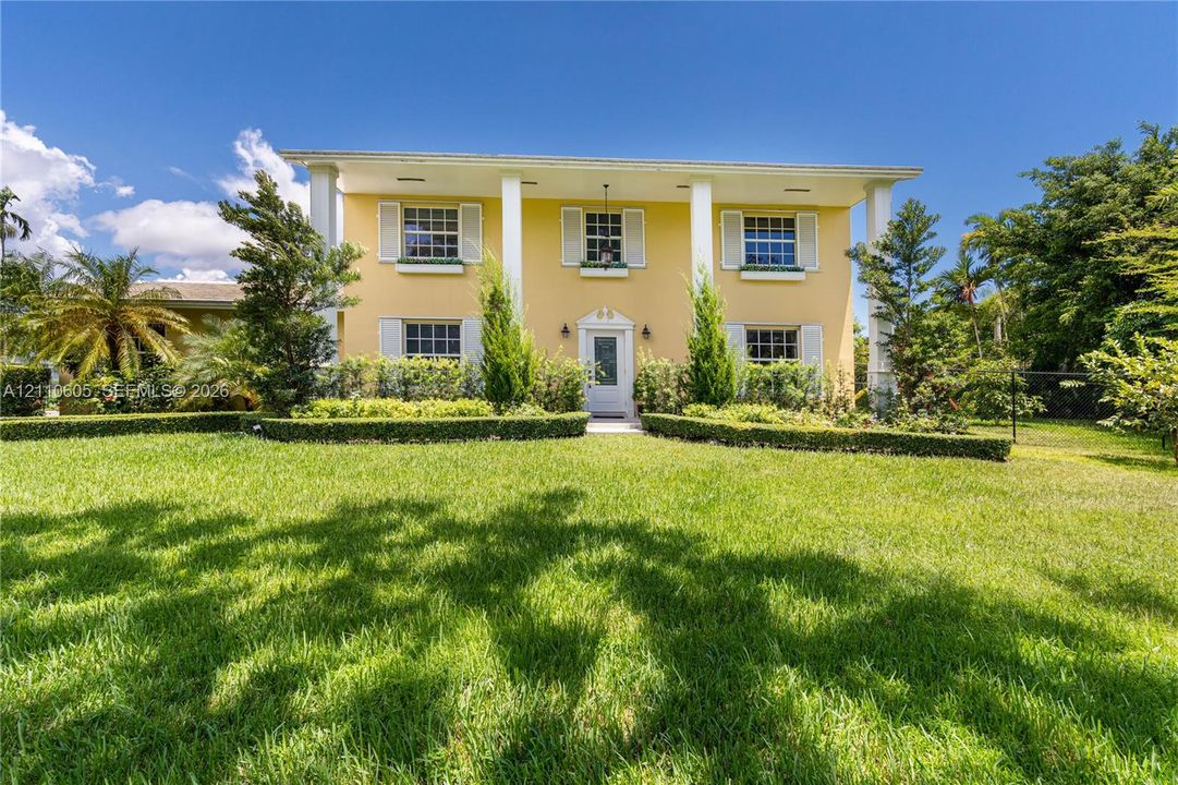 Two-story Colonial-style exterior featuring structural columns, decorative window shutters, window boxes, and manicured landscaping