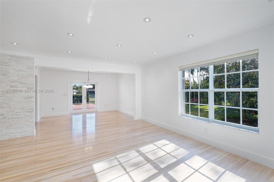 Light-filled interior featuring wood-finish flooring, recessed lighting, a stone-textured accent wall, multi-pane windows, and glass-paned double doors