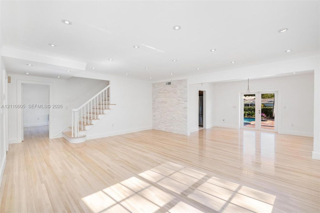 Open-concept interior featuring light wood-finish flooring, recessed lighting, a stone-accented wall, and white staircase railing