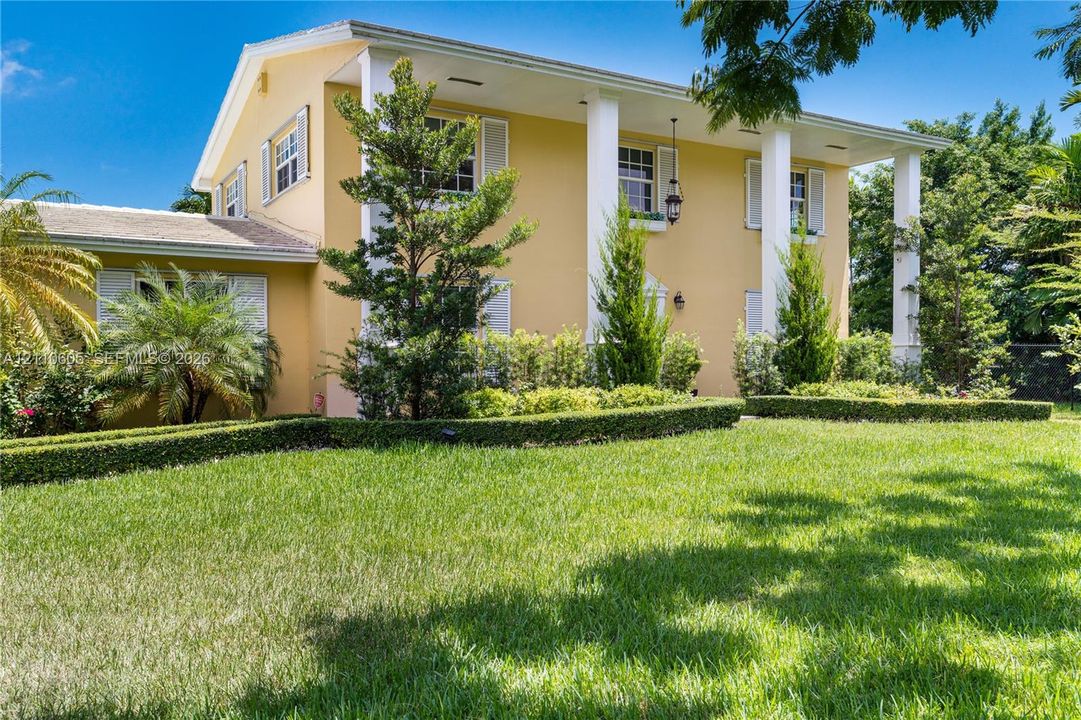 Two-story exterior featuring a covered front porch with white structural columns, louvered window shutters, and manicured landscaping