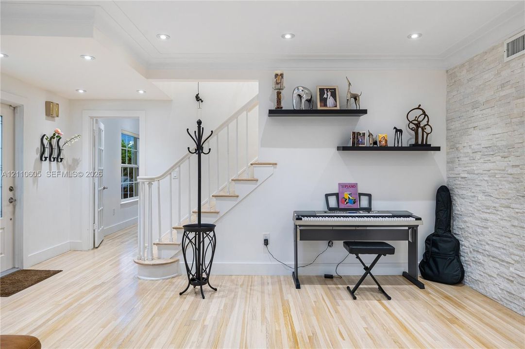 Light wood-finish flooring, textured stone accent wall, recessed lighting, and a staircase with a wooden handrail and balusters