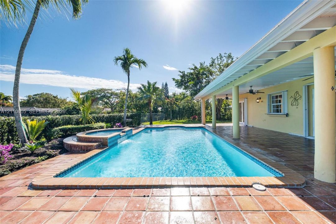 Covered patio featuring a ceramic tile floor and ceiling-mounted fans, overlooking a swimming pool with an integrated raised spa and brick-finished coping